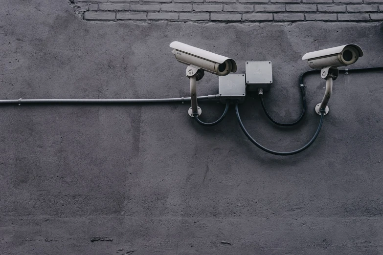 two surveillance cameras mounted on the side of a building, by Jens Søndergaard, pixabay, street art, broken down grey wall, pipe, secuirty cam footage, on a black wall