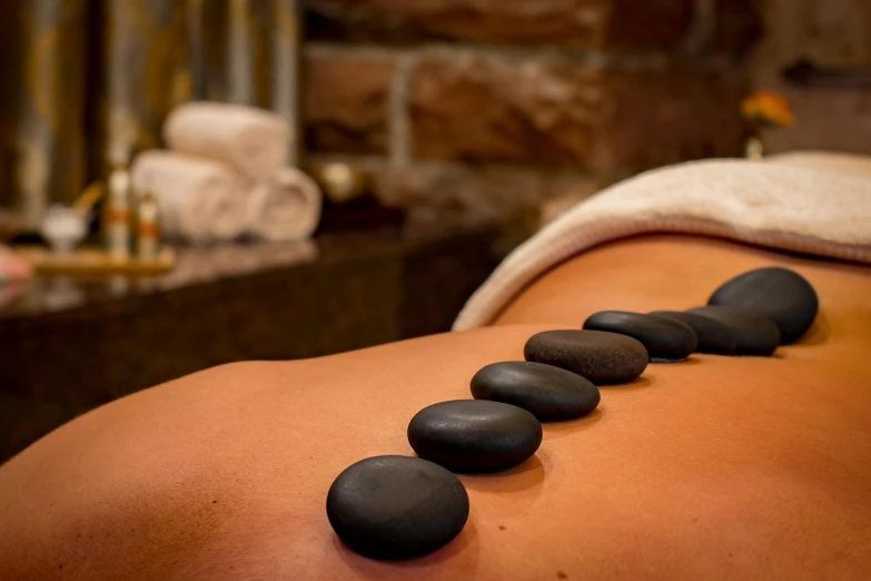 a woman getting a hot stone back massage, pixabay, photo realistic, brown cobble stones, hotel room, black pearls