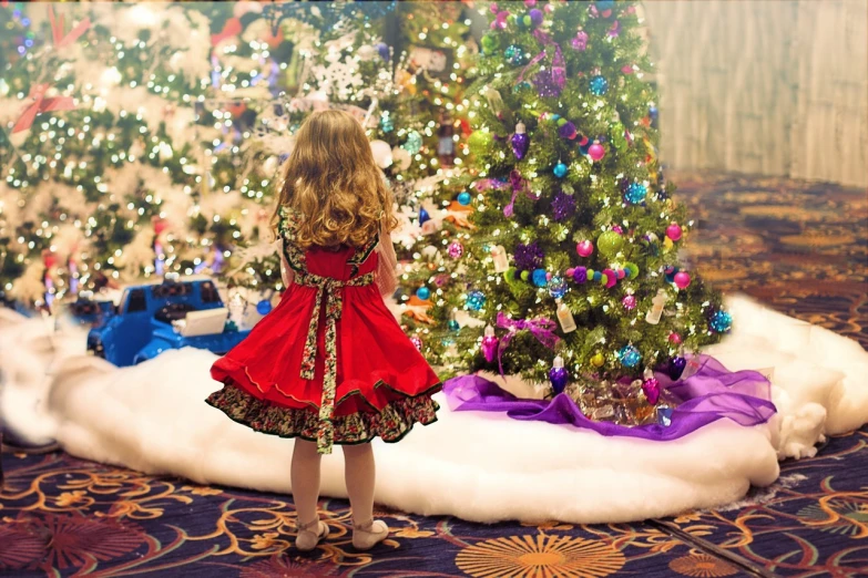 a little girl standing in front of a christmas tree, a photo, by Paul Emmert, shutterstock, award - winning photo. ”