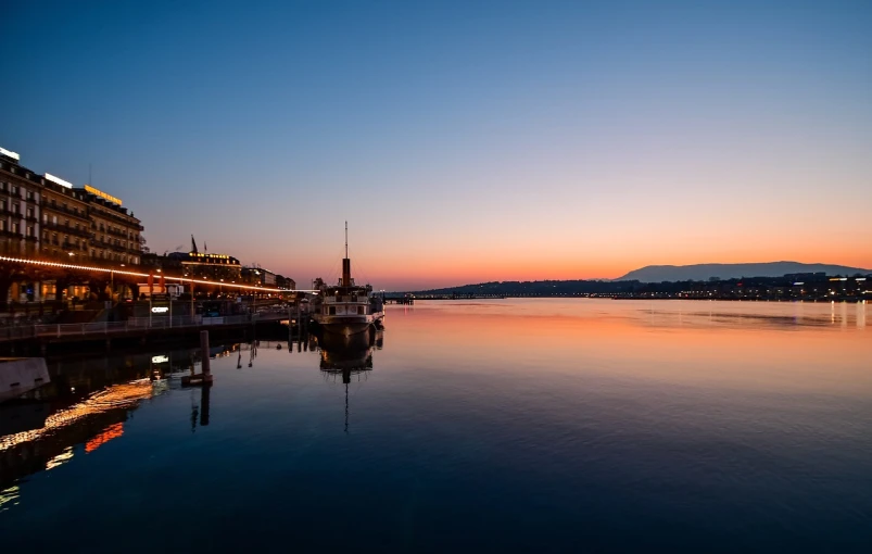 a large body of water next to a tall building, by Alexander Bogen, shutterstock, peaceful evening harbor, switzerland, shot with a canon 20mm lens, beautiful sunrise