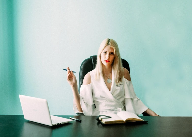 a woman sitting at a desk with a laptop and a pen, a portrait, by Zofia Stryjenska, pexels, minimalism, portrait of a blonde woman, wearing white suit, funny professional photo, modern fantasy