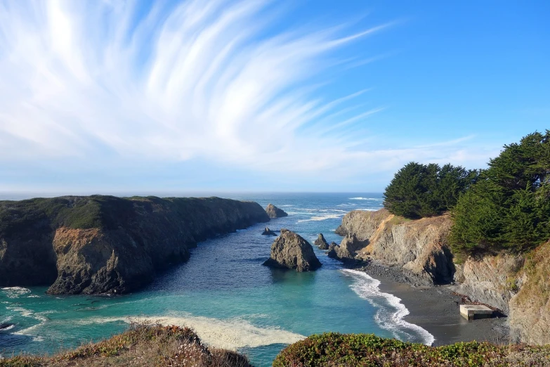 a large body of water sitting on top of a lush green hillside, by Jim Nelson, pexels, california coast, harmony of swirly clouds, rock arcs, beach on the outer rim