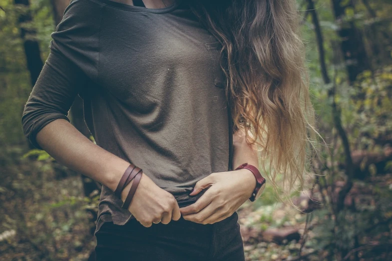 a woman standing in the woods with her hands in her pockets, pexels, renaissance, bangles, wet tshirt, brown color, close up to a skinny