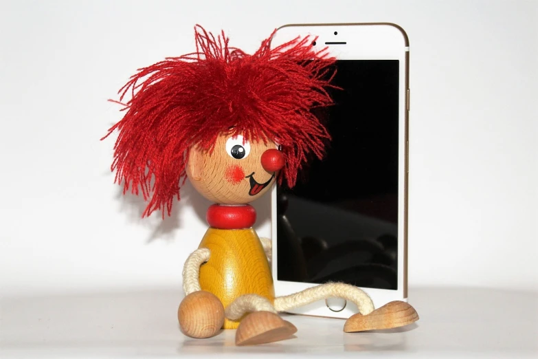 a wooden doll sitting next to a cell phone, a picture, figuration libre, red clown nose, fluffy ebay product, detailed picture, iphone picture