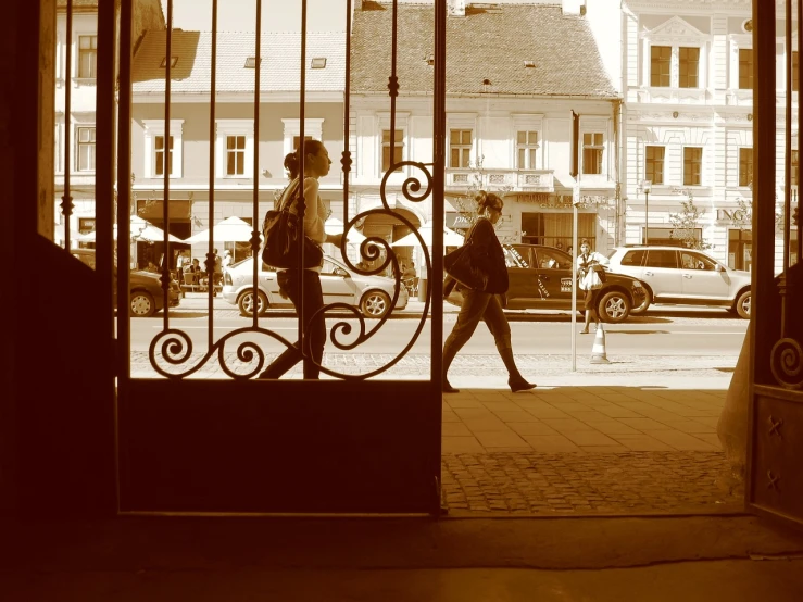 a couple of people that are walking through a door, by Ferenc Joachim, flickr, arabesque, in a city square, sepia sunshine, iron gate, people at work