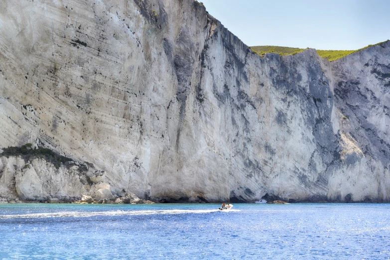 a man riding a surfboard on top of a body of water, a photo, by Simon Marmion, shutterstock, chalk cliffs above, greek fantasy panorama, detailed zoom photo, photo taken from a boat