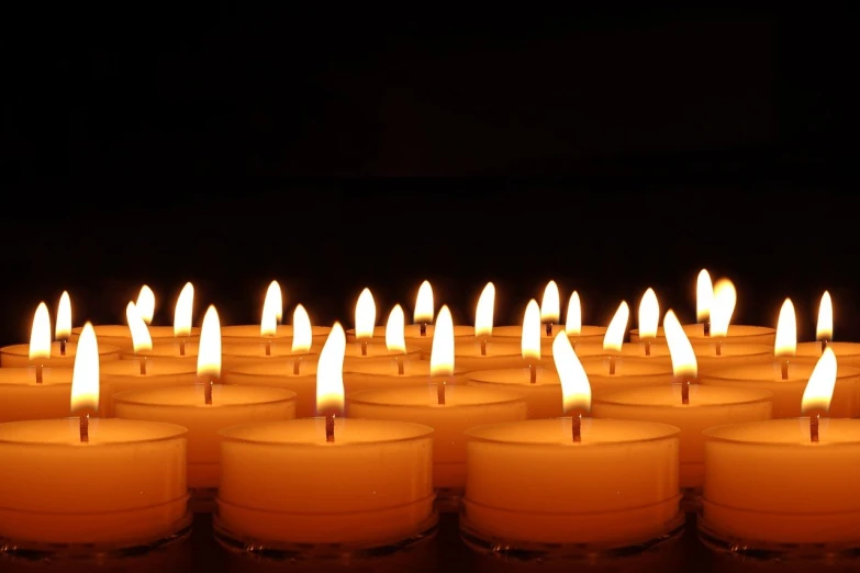 a group of lit candles sitting on top of a table, by Rhea Carmi, pexels, digital art, in front of a black background, istockphoto, remembrance, warm volumetric lights
