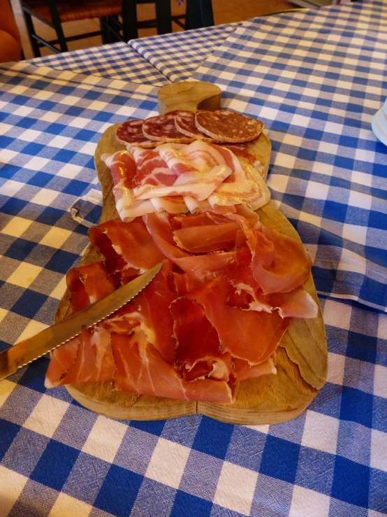 a wooden cutting board topped with meat on top of a blue and white checkered tablecloth, by Antonio Saura, salami, in the dolomites, photo taken in 2018, pink