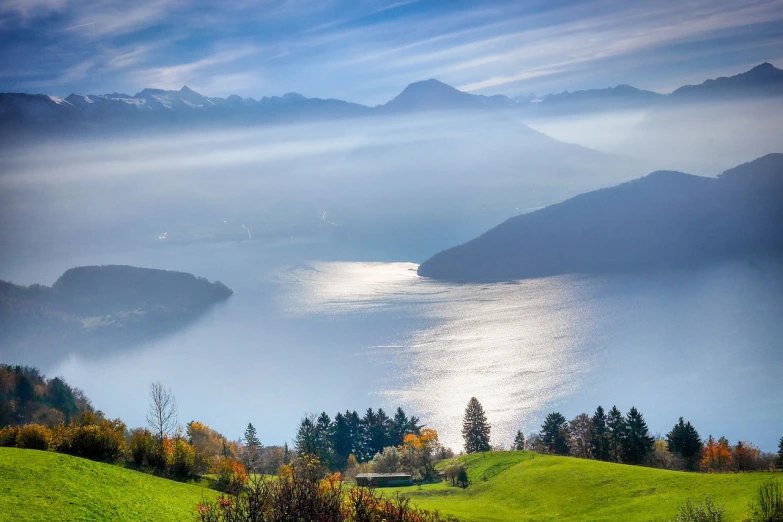 a large body of water sitting on top of a lush green hillside, by Robert Griffier, shutterstock, winter mist around her, swiss, vibrant light, bay