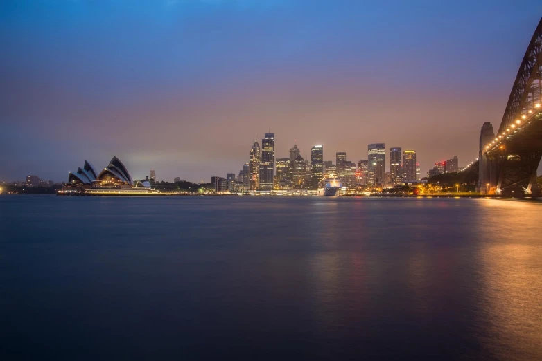 a bridge over a body of water with a city in the background, inspired by Sydney Carline, pexels, hurufiyya, long exposure photo, predawn, dingy, foreground focus