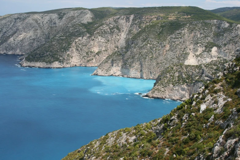 a large body of water sitting on top of a lush green hillside, a picture, hurufiyya, greek nose, blue waters, alexandros pyromallis, sharp cliffs