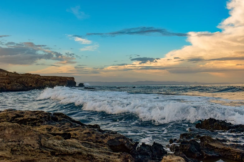 a man standing on top of a rock next to the ocean, by Niklaus Manuel, shutterstock, sunset panorama, rough waves, puerto rico, wide panoramic shot