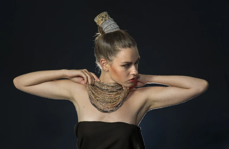 a woman in a black dress posing for a picture, by Siona Shimshi, hair jewellery, scarf made from spaghetti, topknot, golden and silver jewerly