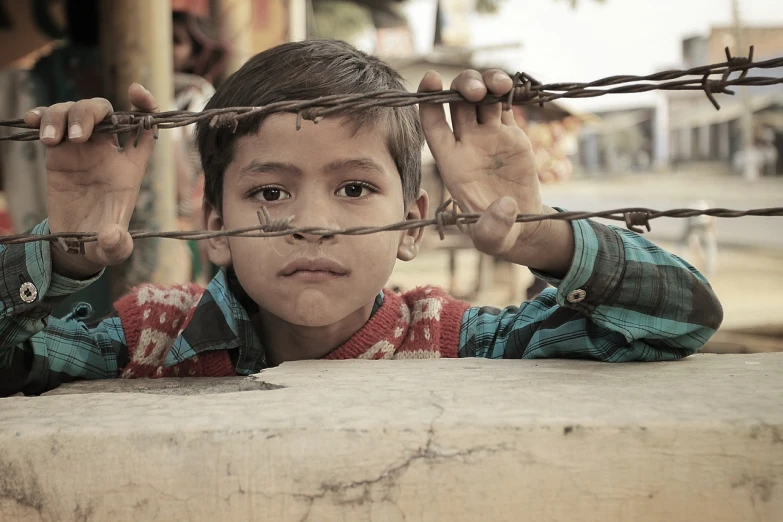 a young boy standing behind a barbed wire fence, a picture, by Saurabh Jethani, pexels contest winner, realism, on an indian street, nostalgic 8k, pretty face!!, bottom angle