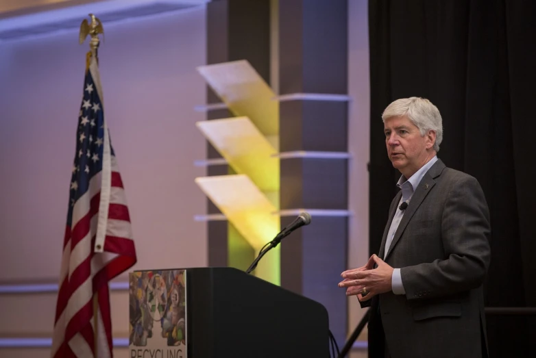 a man standing at a podium in front of an american flag, convention photo, sap, michigan, greg rutowski