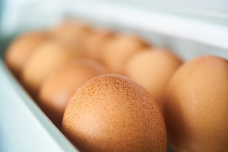 a box filled with brown eggs sitting on top of a table, a pastel, by Yi Jaegwan, shutterstock, happening, close-up shot taken from behind, stock photo, profile close-up view, high grain