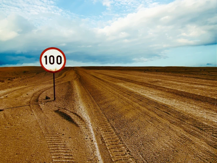 a red and white sign sitting on the side of a dirt road, a stock photo, shutterstock, fine art, sign that says 1 0 0, speed, in russia, oil dereks on horizon