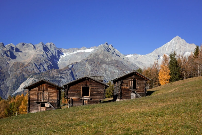 a couple of cabins sitting on top of a grass covered hillside, a picture, by Werner Andermatt, shutterstock, autum, movie set”, glacier, wooden