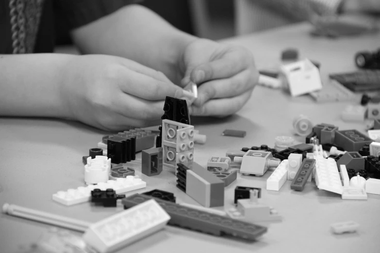 a person sitting at a table with a bunch of legos, a black and white photo, workshop, high detailed photo, playing, product introduction photo