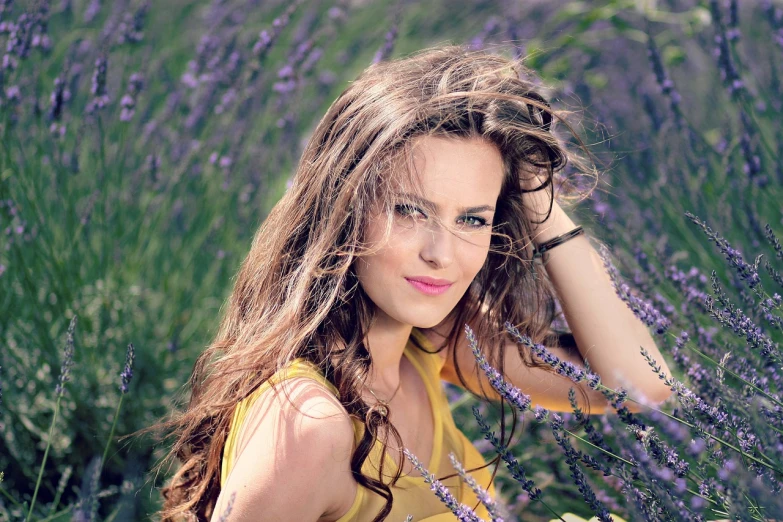 a woman sitting in a field of purple flowers, a picture, by Zofia Stryjenska, shutterstock, long wavy brunette hair, lavander and yellow color scheme, smiling fashion model face, postprocessed)