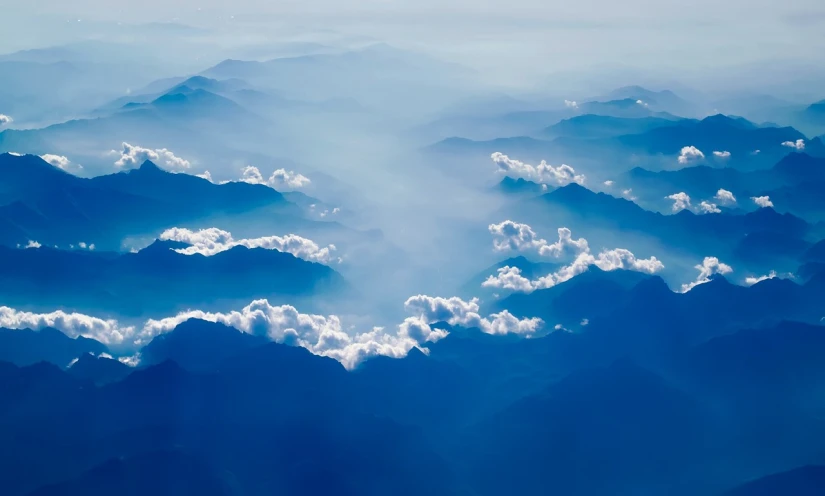 a view of mountains and clouds from an airplane, shutterstock, minimalism, clouds of vivid horse-hair wigs, mystical blue fog, smoke fog and crepuscular rays, dynamic blue sky