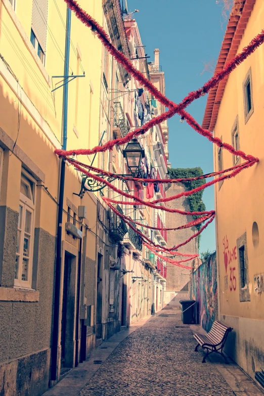 a couple of benches sitting on top of a cobblestone street, a photo, inspired by João Artur da Silva, shutterstock, street art, red wires wrap around, vintage color photo, ribbons and flowers, leading to a beautiful