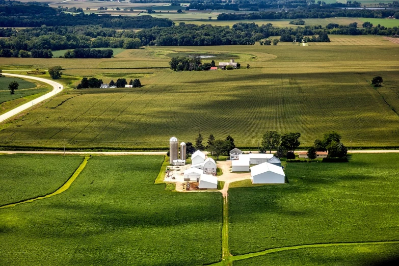 a large white barn sitting on top of a lush green field, a stock photo, by Arnie Swekel, view from the top, midwest town, shot on nikon z9, liquid gold