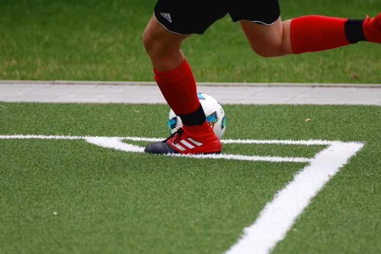 a person kicking a soccer ball on a field, by Christen Dalsgaard, pixabay, figuration libre, red boots, detailed zoom photo, on a football field, indoor shot
