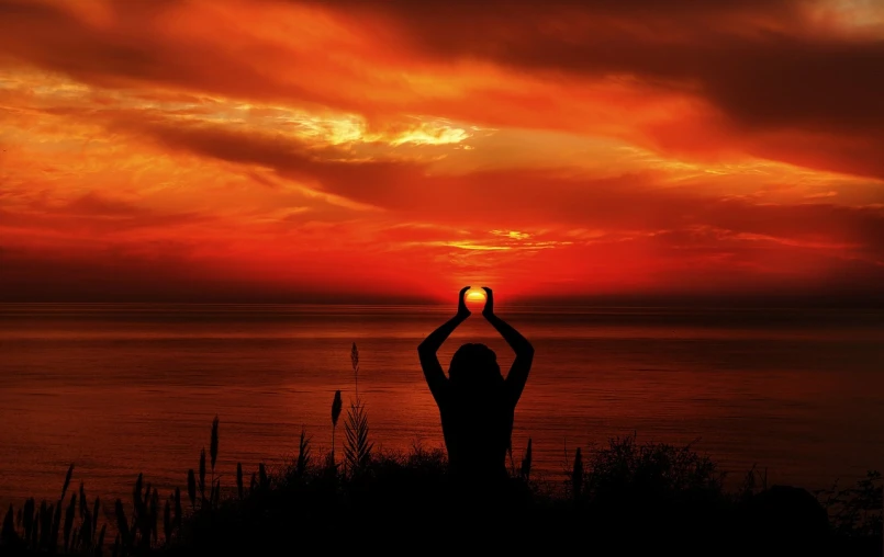 a person standing in front of a sunset with their hands in the air, a picture, by Jan Rustem, romanticism, a woman holding an orb, red reflective lens, peace and love, silhuette