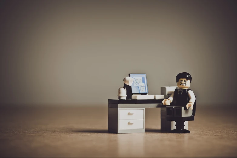 a lego man sitting at a desk with a computer, a tilt shift photo, by Karl Buesgen, postminimalism, officer, display”