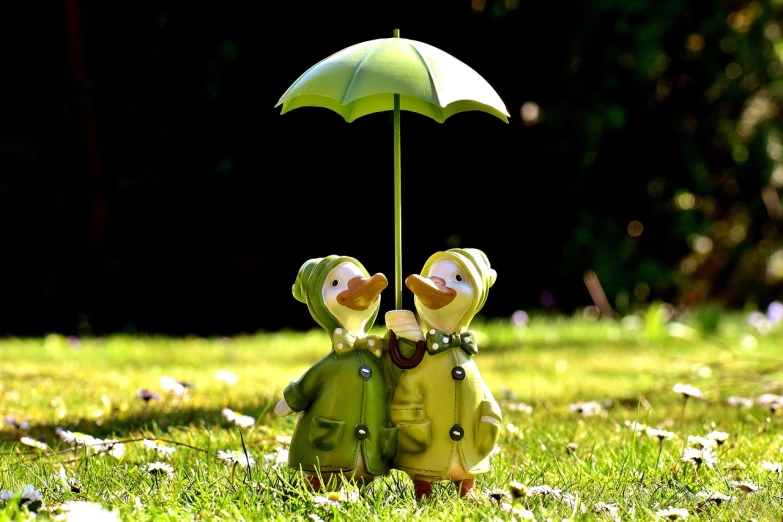 a couple of figurines sitting on top of a lush green field, a picture, by Armin Baumgarten, pixabay, umbrella, subject= duck, full of greenish liquid, twins