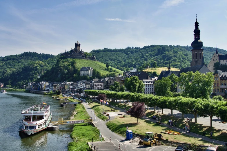 a large boat sitting on top of a river next to a lush green hillside, a photo, by Robert Zünd, pexels, plein air, in the foreground a small town, berkerk, germany. wide shot, istock