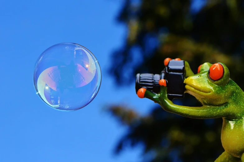 a frog figurine holding a camera and blowing a bubble, a picture, by Jan Rustem, pexels, precisionism, rainbow bubbles, view from below, soap bubble, 2 0 5 6