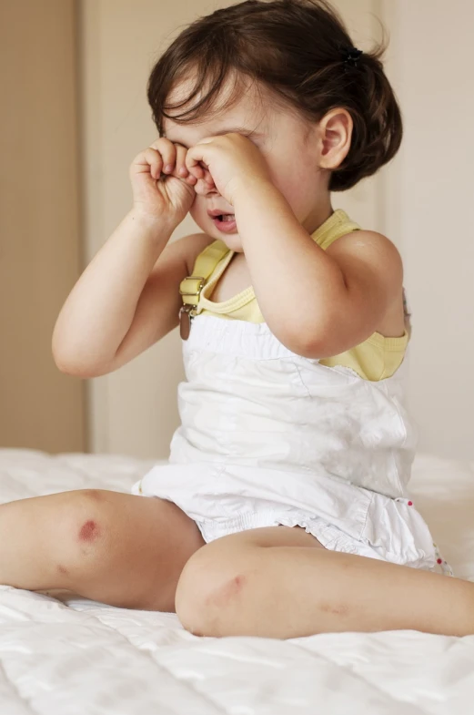 a little girl sitting on top of a bed covering her eyes, a picture, high res photo, sweating, 2 years old, knee