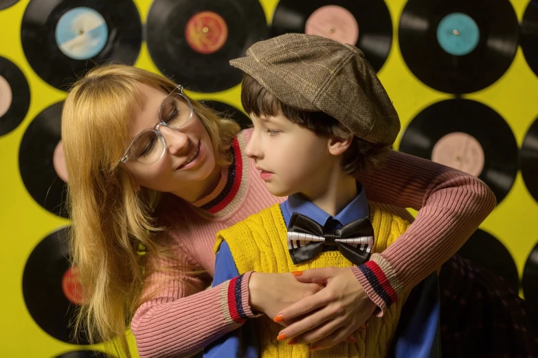 a woman hugging a young boy in front of a wall of records, a portrait, de stijl, soft portrait shot 8 k, retro - vintage, girl wearing round glasses, portrait of a patchwork boy