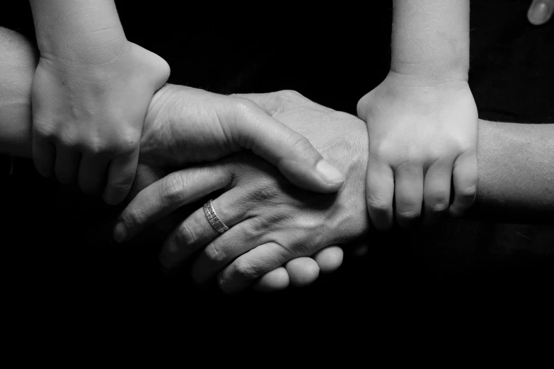 a black and white photo of a group of people holding hands, by Mirko Rački, flickr, high detail of a hand, husband wife and son, support, with a black background