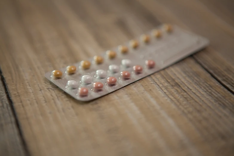 a pill pack sitting on top of a wooden table, shutterstock, antipodeans, het meisje met de parel, varying dots, gradient brown to silver, femme fetal