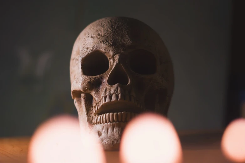 a skull sitting on top of a table next to candles, a portrait, pexels contest winner, closeup 4k, stock photo, soft warm light, close up shot of an amulet
