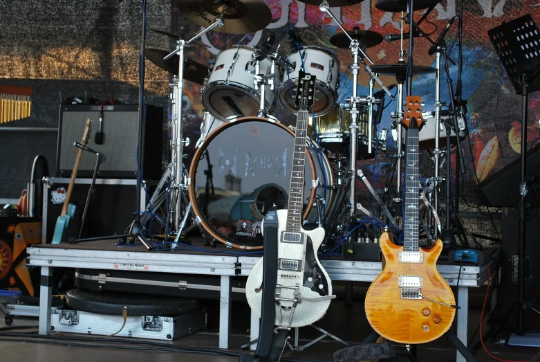 a group of guitars sitting on top of a stage, by Tom Carapic, closeup!!!!!!, covered outdoor stage, flash photo, very wide view