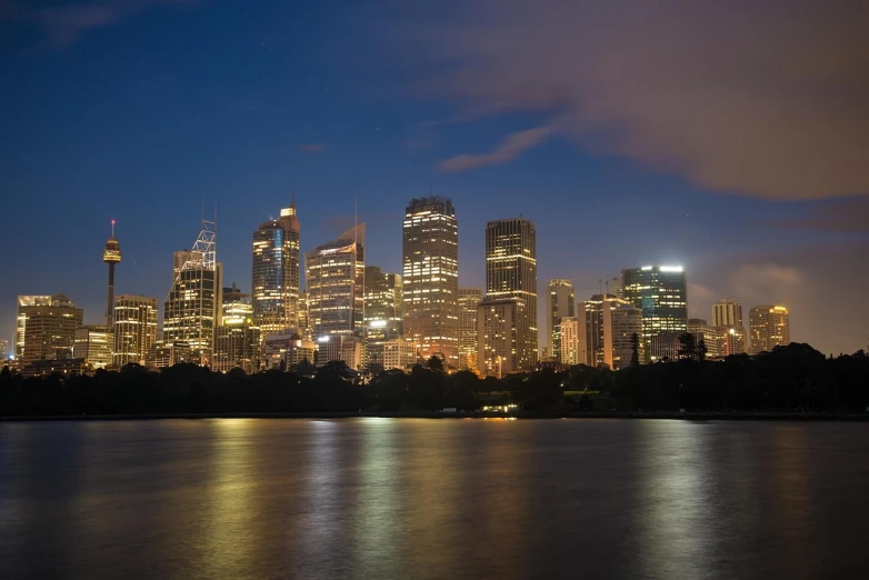 a large body of water with a city in the background, inspired by Sydney Carline, hurufiyya, night life buildings, wikimedia, flash photograph, ( greg rutkowski )