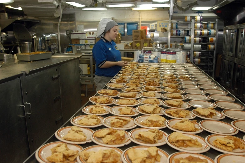 a woman standing in front of a counter filled with plates of food, by Bradley Walker Tomlin, flickr, shipgirls, apple pie, factory floor, islands!!!!!