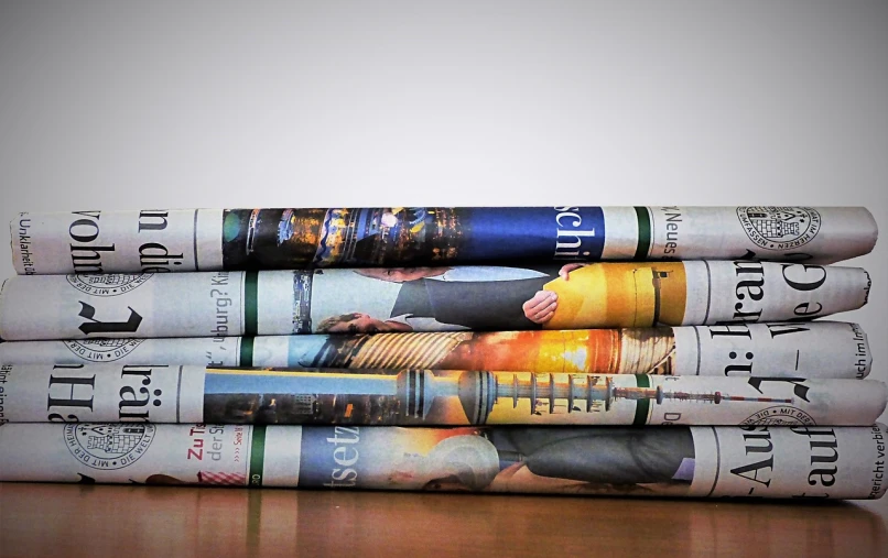 a stack of newspapers sitting on top of a wooden table, a picture, by Stefan Gierowski, pixabay, private press, spines, tubes, coloured photo, backlit