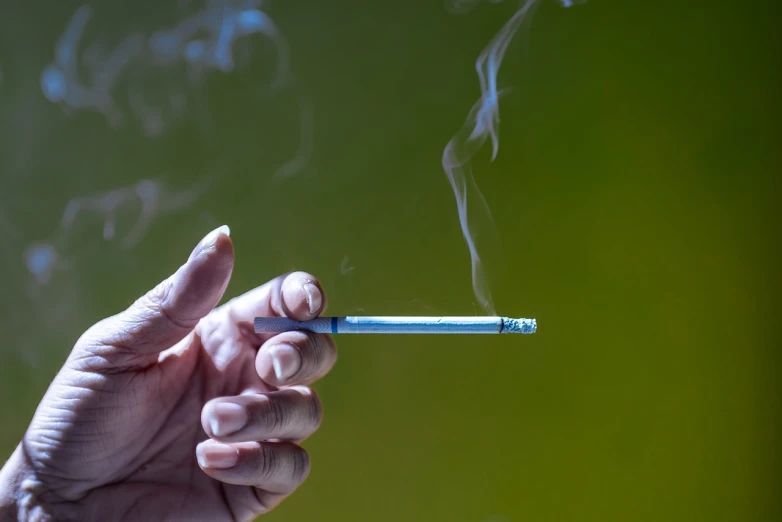 a hand holding a cigarette with smoke coming out of it, by Richard Carline, happening, a green, high detailed photo, at noon, educational