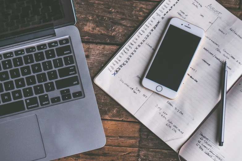 a cell phone sitting on top of a notebook next to a laptop, a picture, by Romain brook, pexels, planning, bottom angle, grungy, organized