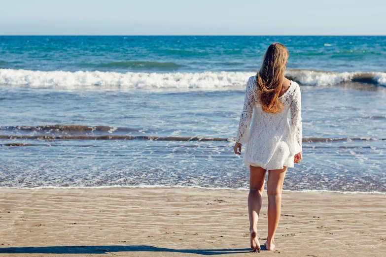 a woman standing on top of a sandy beach, pixabay, wearing a wet white short dress, walking to the right, girl looking at the ocean waves, bright sunny day