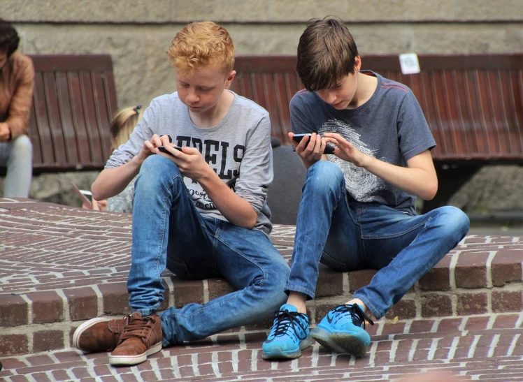 two boys sitting on steps looking at their cell phones, a photo, pexels, incoherents, red haired teen boy, digging, 1505, twins playing video games