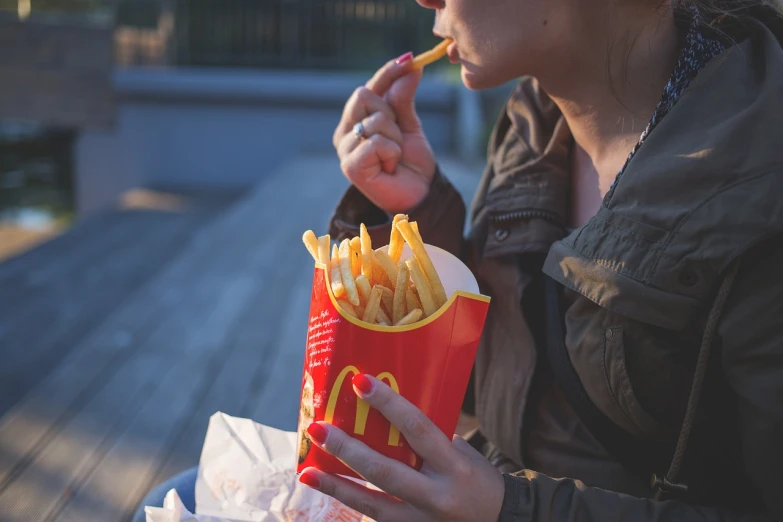 a woman sitting on a bench eating french fries, pexels, realism, mc donalds, stock photo, close-up shot, with a straw