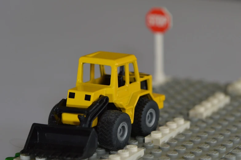 a toy bulldozer sits in front of a stop sign, by Viktor Oliva, flickr, lego, jcb, accurate roads, detailed zoom photo