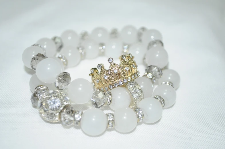 a close up of a bracelet with a crown on it, by Aya Goda, tumblr, bright white castle stones, stacked, glossy white, queen of heaven