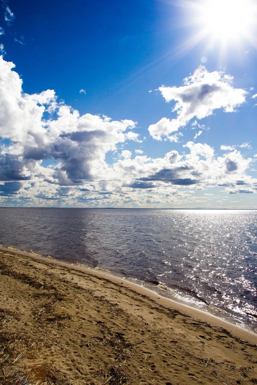 a bench sitting on top of a sandy beach next to the ocean, a photo, by Alexander Fedosav, beautiful sky with cumulus couds, great river, midday sun, vladimir krisetskiy